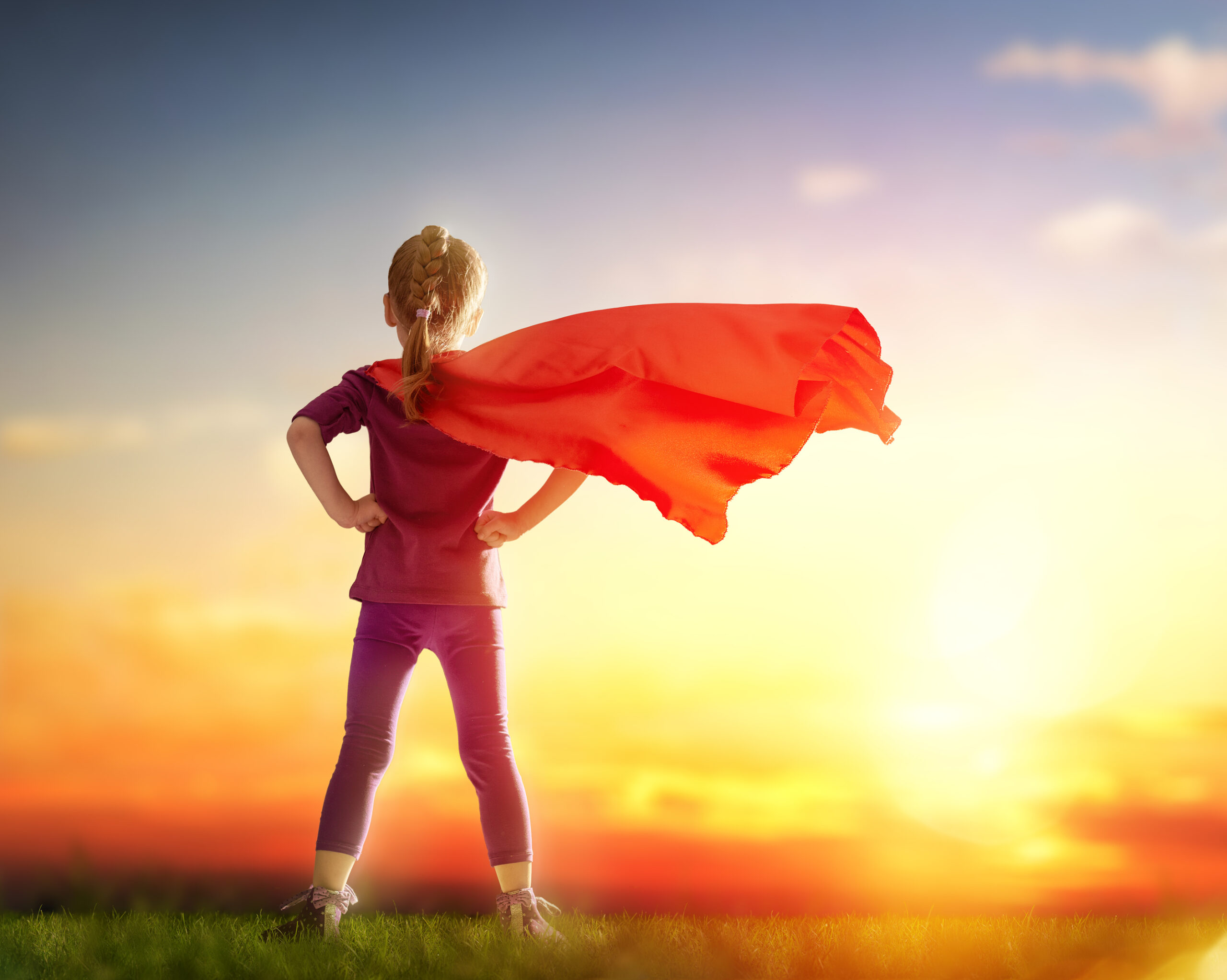 Little child girl plays superhero. Child standing before sunset