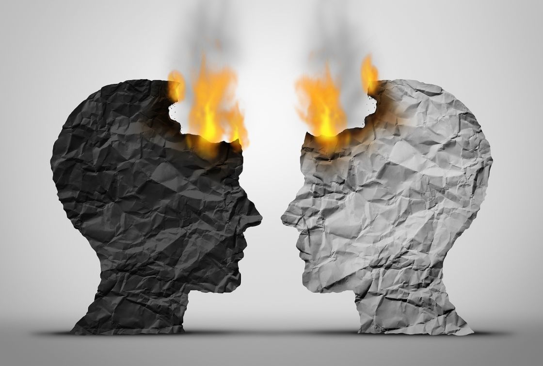 Profiles of Two Faces Made From Paper, One Black and One White, Facing Each Other and Beginning to Catch on Fire