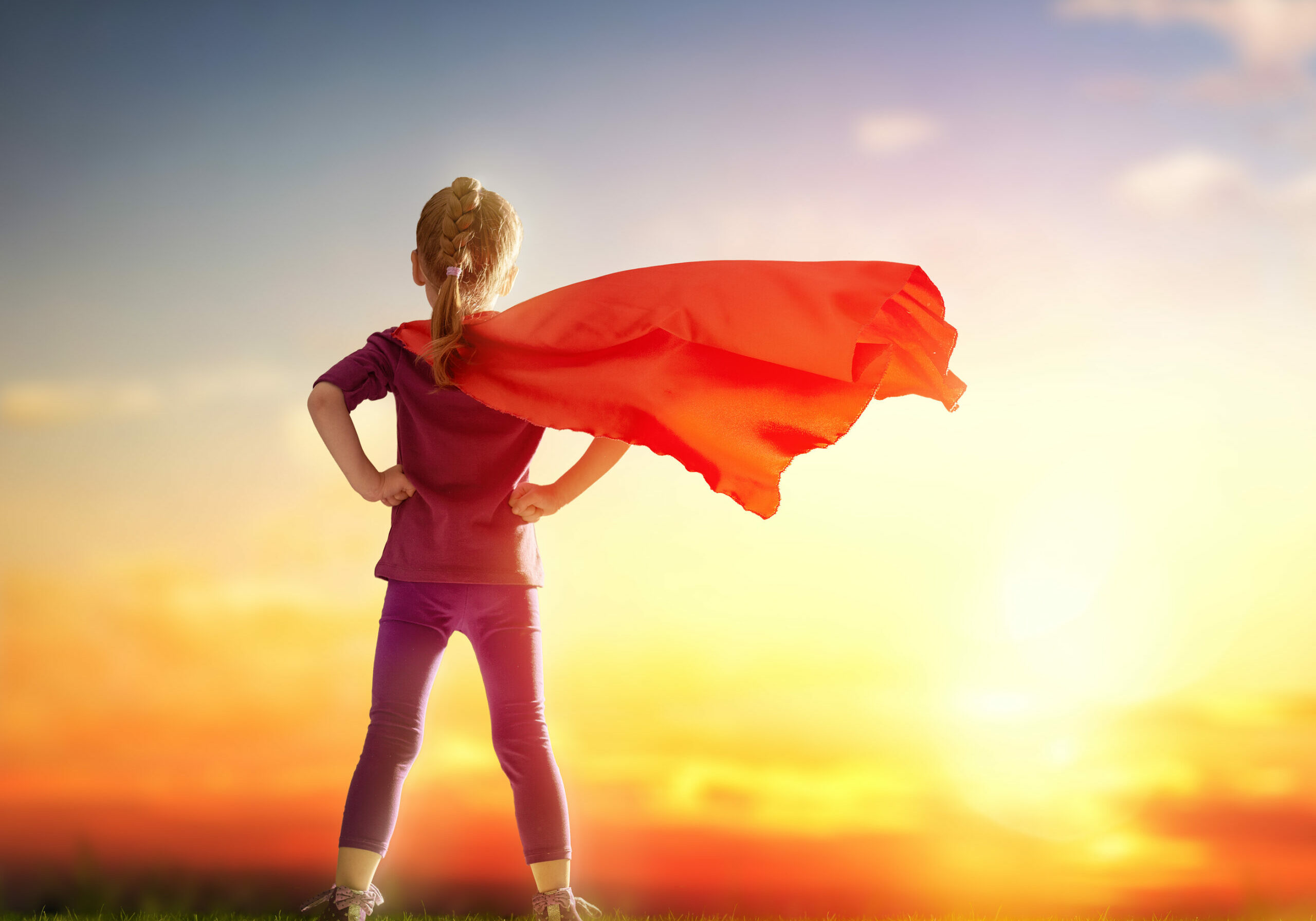 Little child girl plays superhero. Child standing before sunset