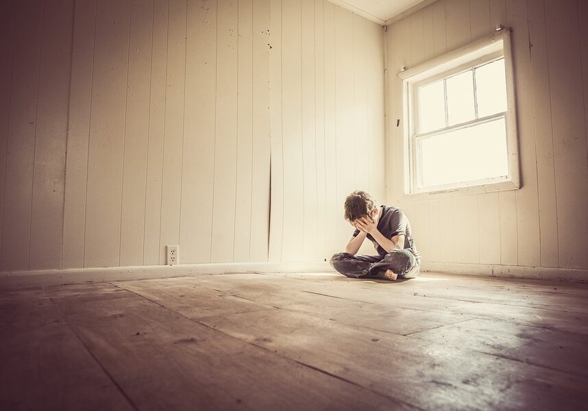 Boy Sitting in Empty Room With Face In HIs Hands