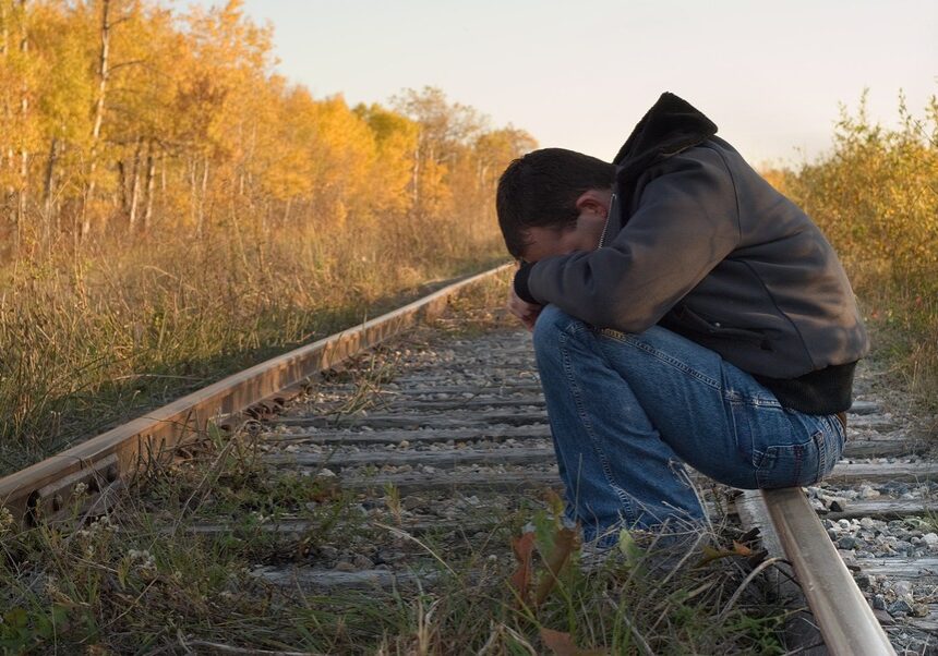 Man With Head Buried in His Lap Sitting on a Railroad Track